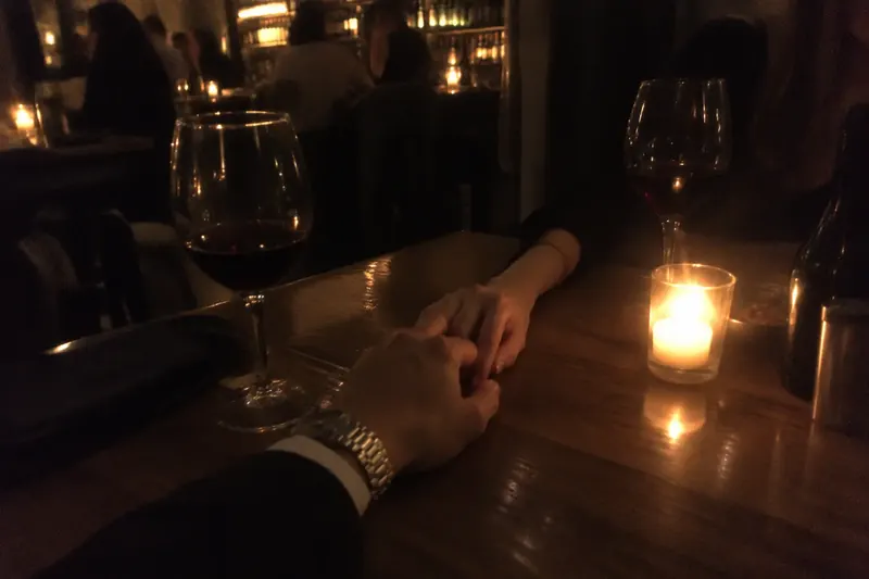 Two hands touching across a candlelit wine bar table