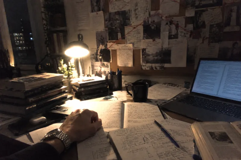 Handwritten notebooks, books and a laptop spread across a desk at night