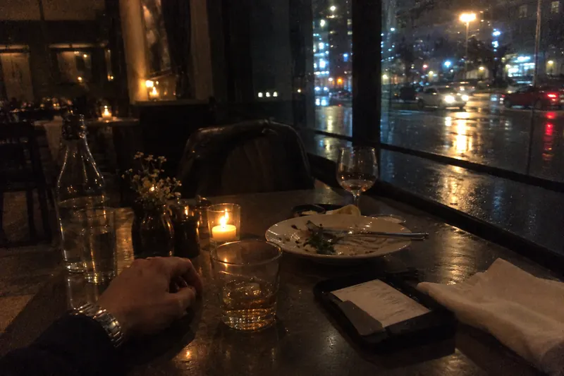 Empty chair at a candlelit restaurant table beside a rainy window